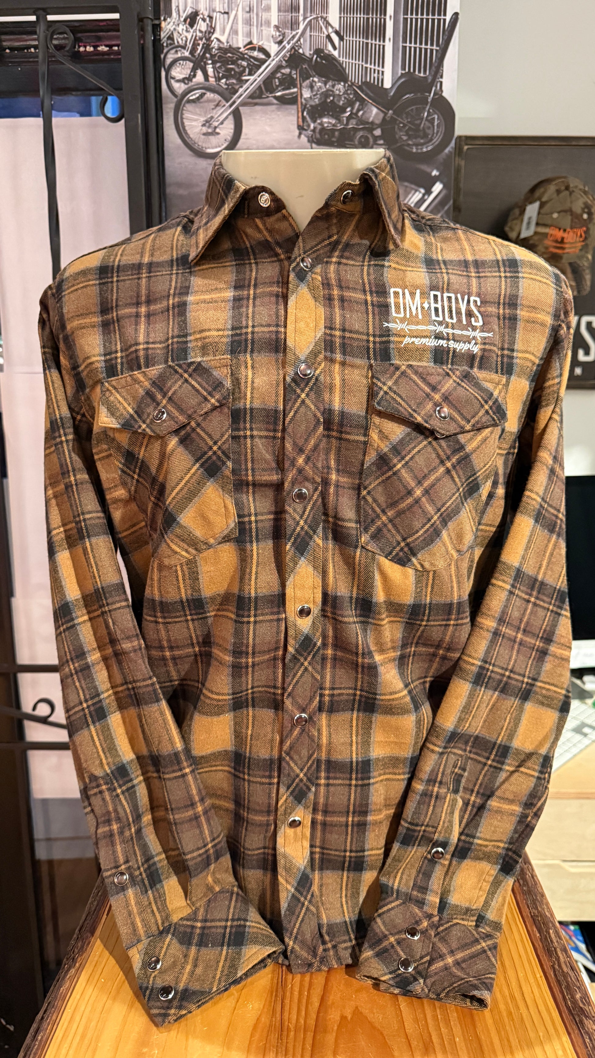 Plaid shirt with 'OMBOYS' logo on a wooden surface