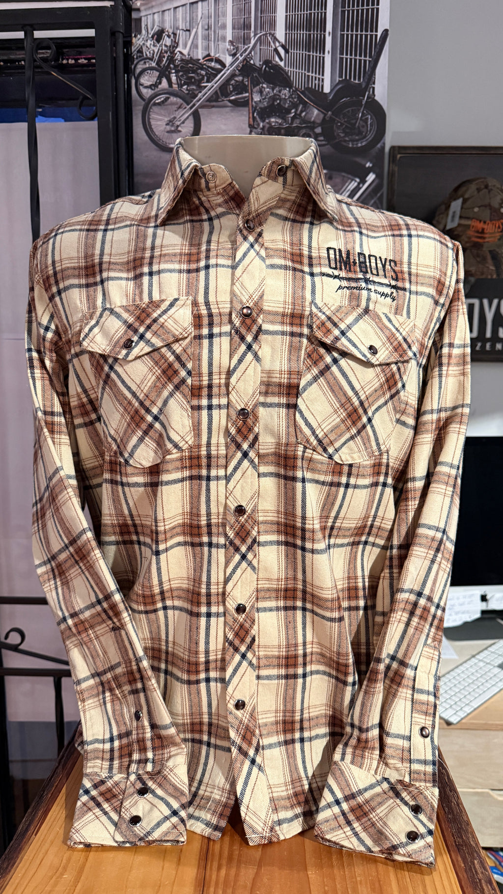Plaid shirt with 'OMBOYS' branding on a wooden surface